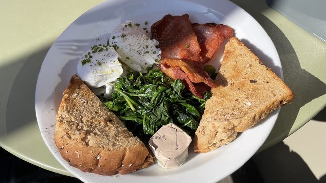 A full brunch plate of poached egg, bacon, spinach, mushrooms and toast