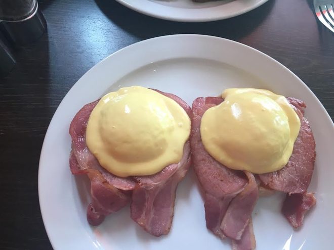 Poached eggs with hollandaise over ham on a white plate