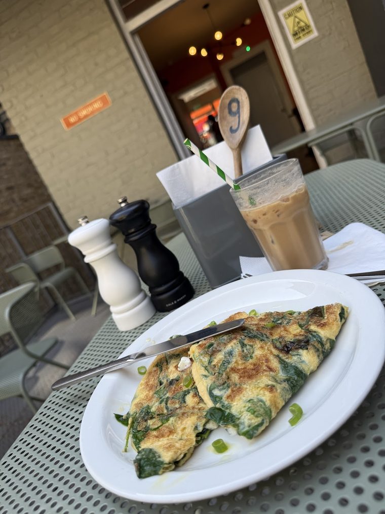 A spinach omelette on an oval plate with an iced coffee behind it